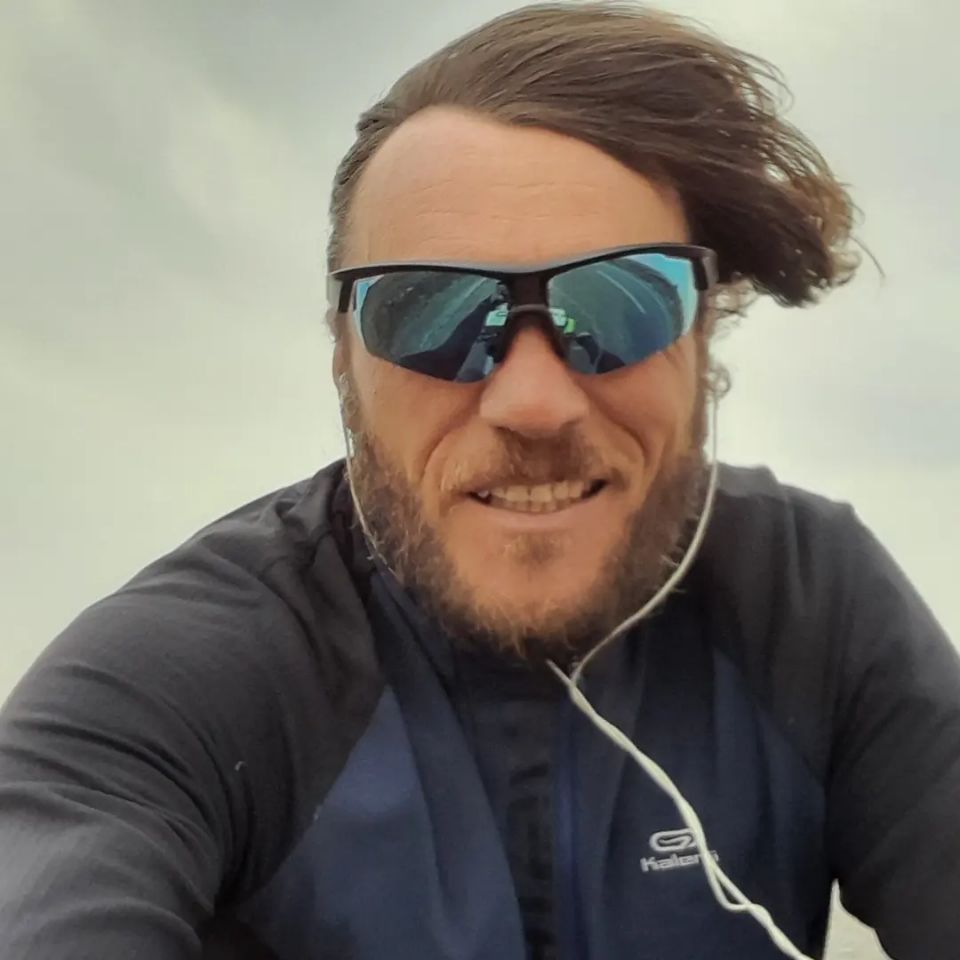 Ich fahre Rad bei starkem Wind, der meine Haare waagerecht nach rechts weht.