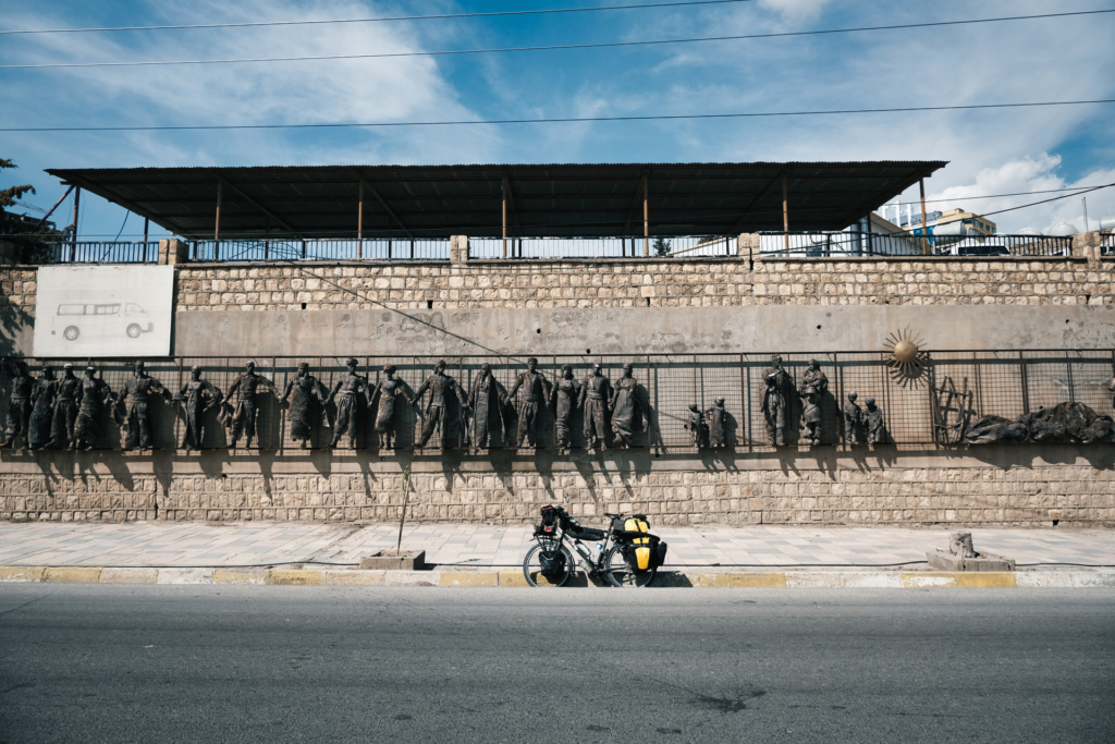 Fahrrad steht vor einer Installation: Eine Reihe Bronzestatuen hält sich Hand in Hand an einer Mauer fest.