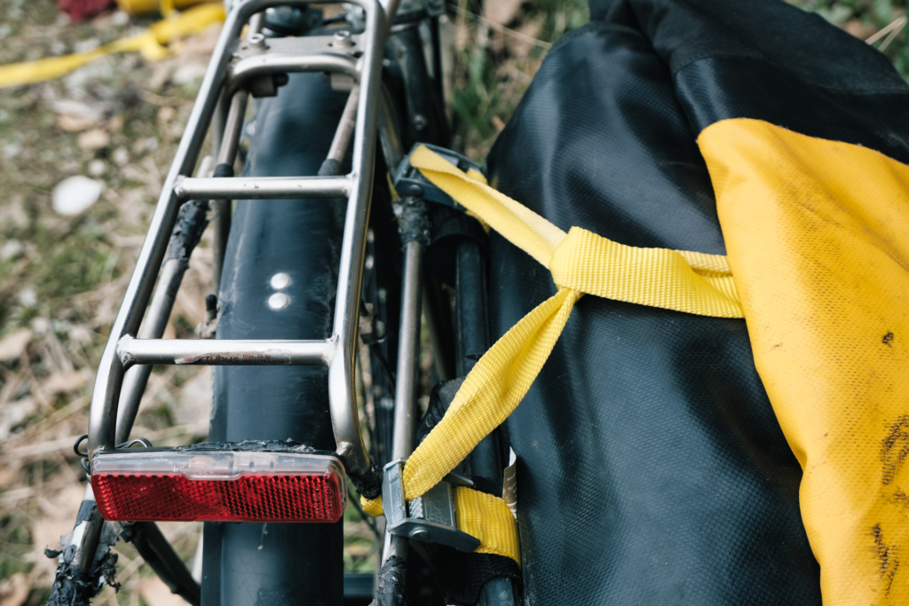 Die Fahrradtaschen sind provisorisch mit gelbem Zurrband am Gepäckträger befestigt