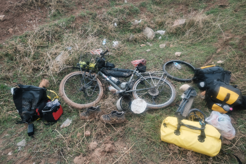 Das Fahrrad liegt am Boden. Taschen und Schuhe liegen daneben, wobei Reifen und Schuhe komplett mit Matsch bedeckt sind