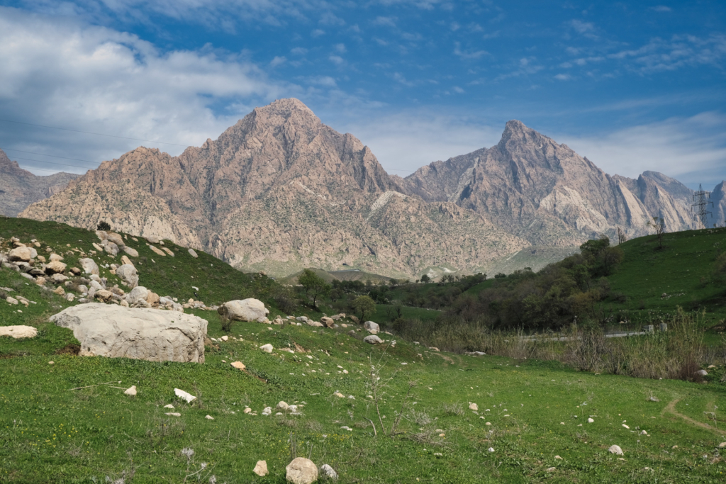 Gewaltiges beiges Bergmassiv ragt hinter saftigen Wiesen voller Findlinge auf