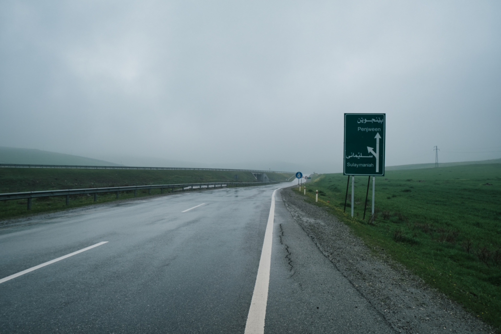 Leere, nasse Straße bei trist-grauem Regenwetter. Ein Straßenschild weist auf Penjween hin.