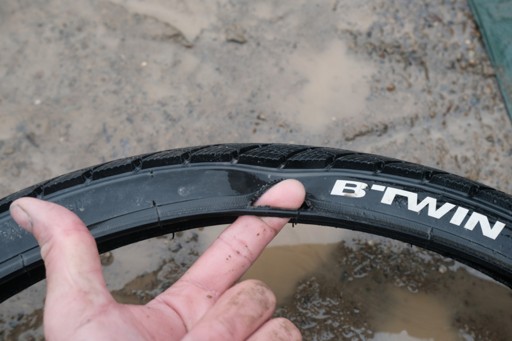 Nahaufnahme eines gerissenen Fahrradreifens: Zur Veranschaulichung des Schadens steckt mein Zeigefinger in der Seitenwand.