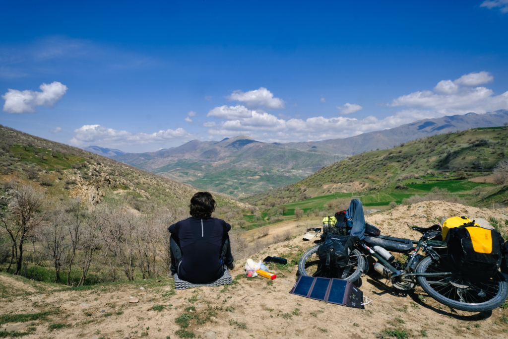 Ich sitze auf dem Pass neben meinem Rad und schaue nach vorne in die Weite der Berge, nachdem ich den Aufstieg geschafft habe.