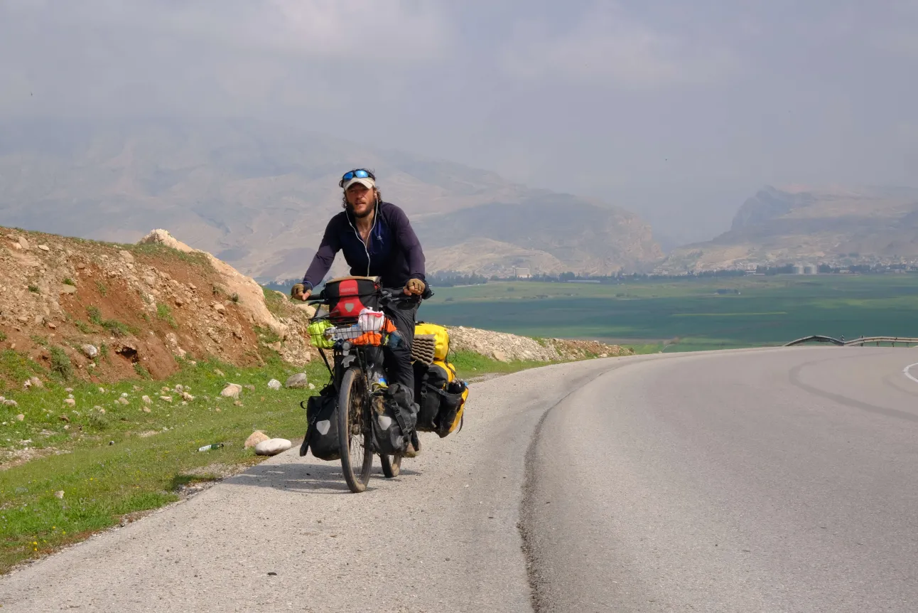Ich fahre mit meinem voll bepackten Tourenrad bergauf auf die Kamera zu. Hinter mir erstreckt sich ein grünes Tal, gerahmt von im Nebel verschlungenen Bergen