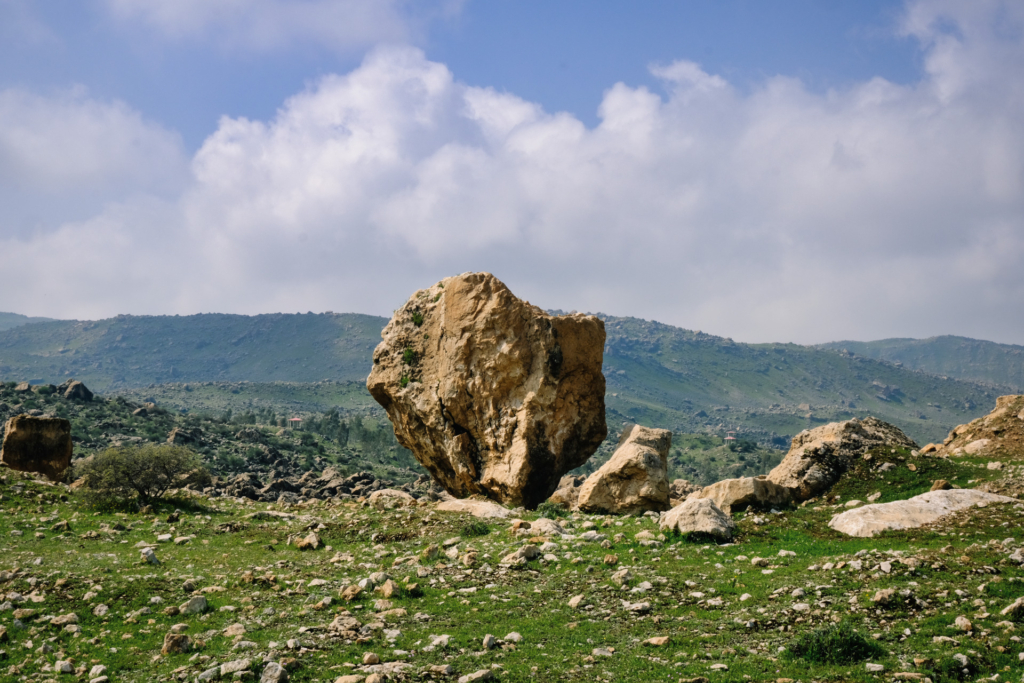 Auf der Wiese steht ein großer beiger Findling, der sich nach unten immer weiter verjüngt