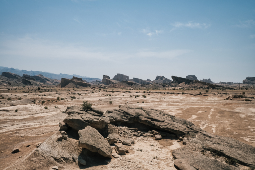 Blick in eine sandige Steinwüste. Am Horizont ragen einzelne Plateauplatten aus der Erde