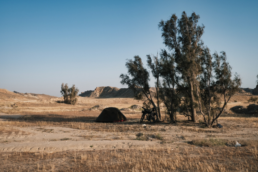 In einer Steppenähnlichen Landschaft steht ein einzelner Baum und in dessen Schatten ist ein Zelt aufgebaut