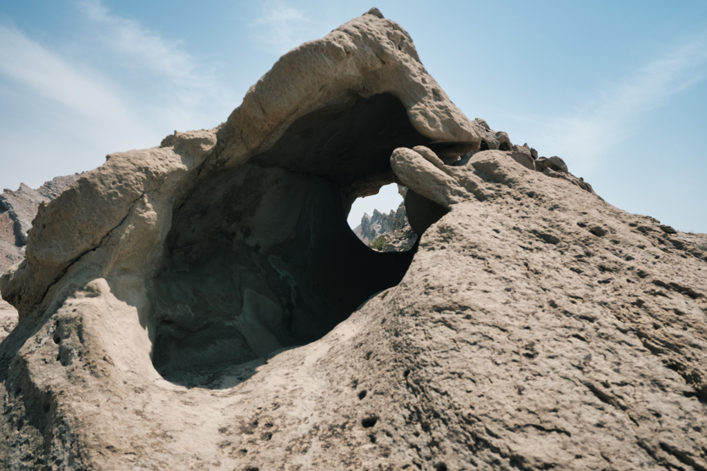 Eine Felsformation in Form eines Tunnels. Wir blicken hindurch auf die Berge im Hintergrund