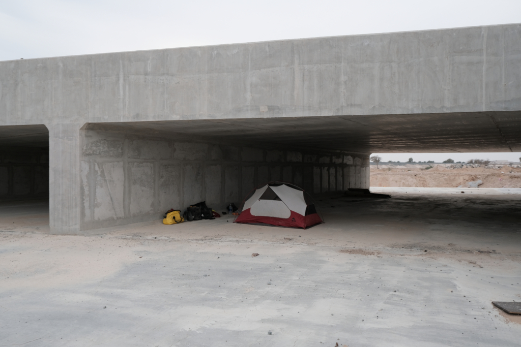 Unter eine Brücke, auf Betonboden steht mein Zelt. Die Taschen liegen daneben.