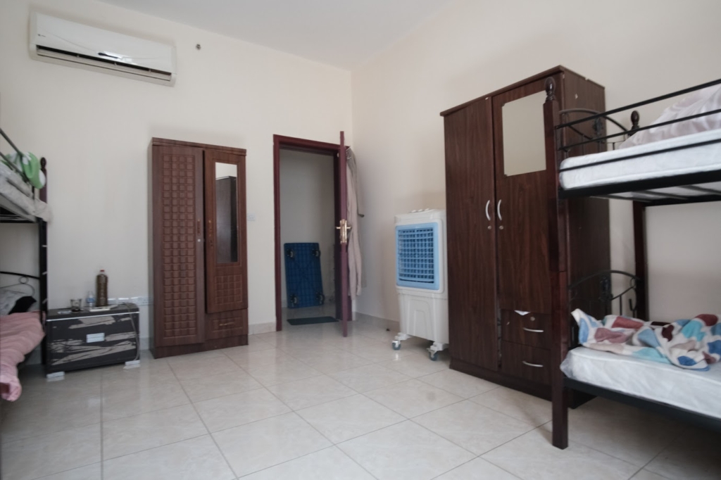 Ein bescheidenes Hostelzimmer. Weißer Boden und Wände, dukelbraune Hochbetten, Schränke und Türen.